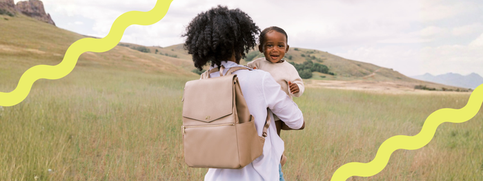 A mom wearing a diaper bag and holding her baby